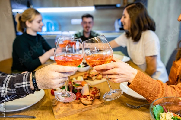 Obraz Group of friends enjoying dinner. Focus on hands having a toast with rose wine.