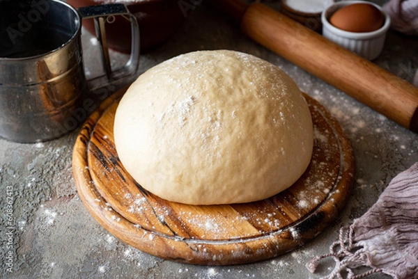 Fototapeta Sweet yeast dough for sweet buns on a wooden board on a gray background. Close-up.