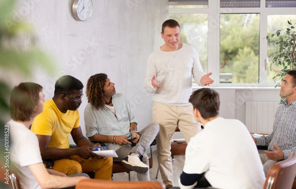 Fototapeta Middle-aged man teacher reading lecture in front of group of guys attending him sitting on chairs