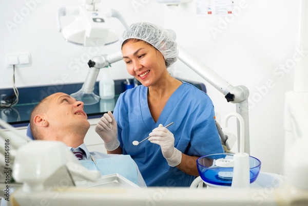 Fototapeta Positive female dentist preparing for a male oral examination