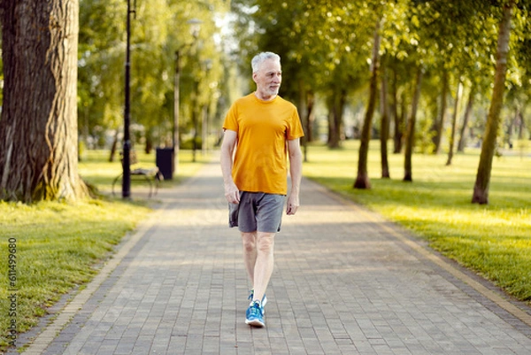 Obraz Senior athletic man walking at the park alley, preparing for the morning training