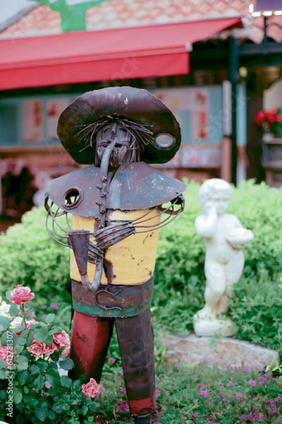 Fototapeta View of abstract garden statue playing saxophone made from iron in garden with defocused background. No people.