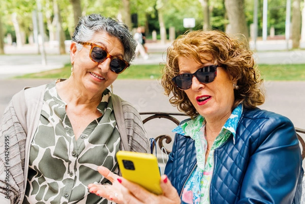 Fototapeta Aged women using mobile phone sitting on a park