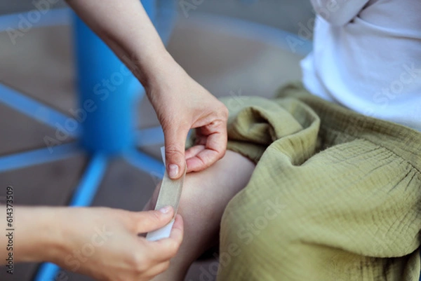 Fototapeta Close-up, sticking a band-aid on a child's leg wound.