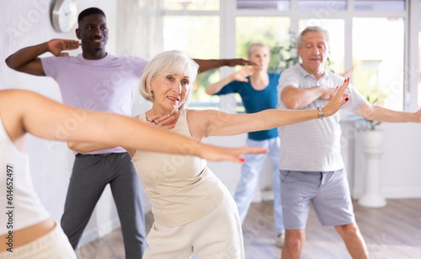 Fototapeta Elderly European woman participate in group dance class. Multinational group of people positively engaged in dance lesson for outdoor enthusiasts.