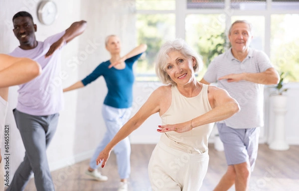 Fototapeta Positive sporty senior woman participating group dance class, practicing modern vigorous energetic dance movements