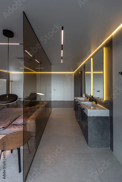 Fototapeta cool expensive interior design of room in prestigious luxury hotel with dark tones with modern LED lighting and stylish furniture. the area with a sink is separated by dark glass from the bedroom