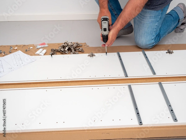 Fototapeta A man assembles furniture at home with a professional screwdriver. Furniture assembly.