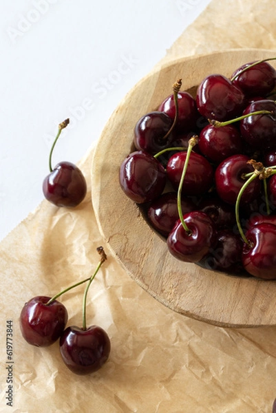 Obraz Cherries in a wooden bowl on brown textured paper on a white table