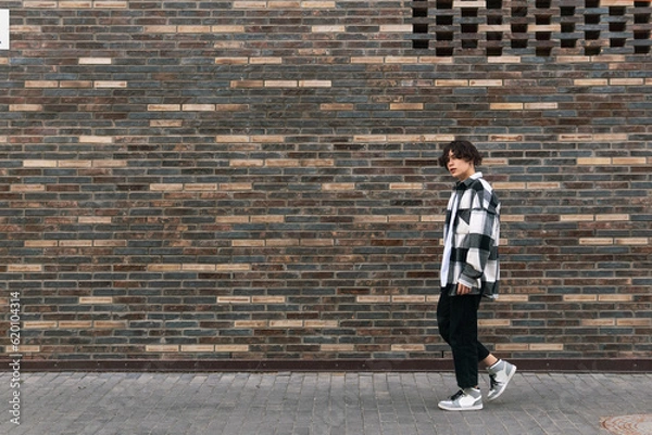 Fototapeta young man walks down the street in front of a brick wall