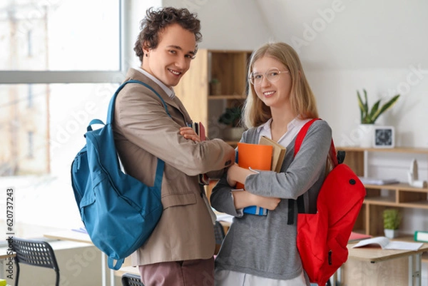 Fototapeta Cute teenage couple with books in classroom