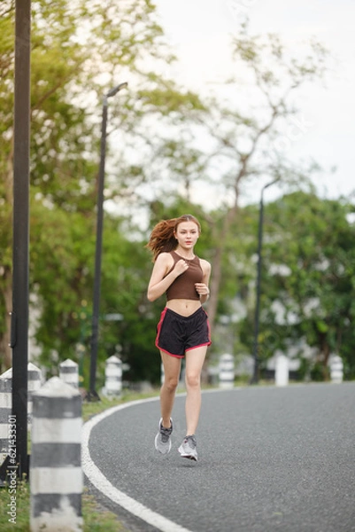 Fototapeta Healthy Asian woman is jogging running outdoor. Sport girl running. Female exercising at outdoor park. Sunset or Sunrise.