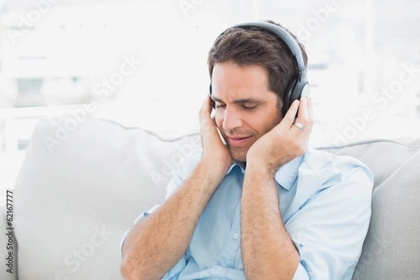 Fototapeta Handsome man sitting on sofa listening to music