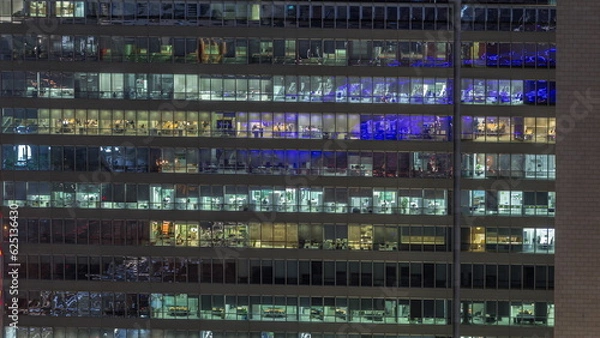 Fototapeta Frontal view of night facade of building with a lot of windows with light timelapse.