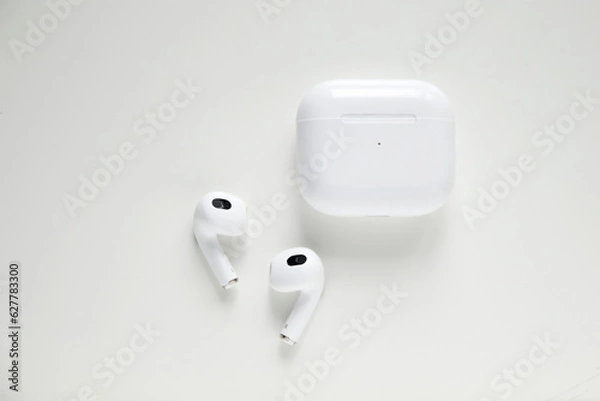 Fototapeta Wireless headphones and charging box on white background. Wireless bluetooth headphones in white case isolated on white background. accessories for listening music or work from home. Out of focus