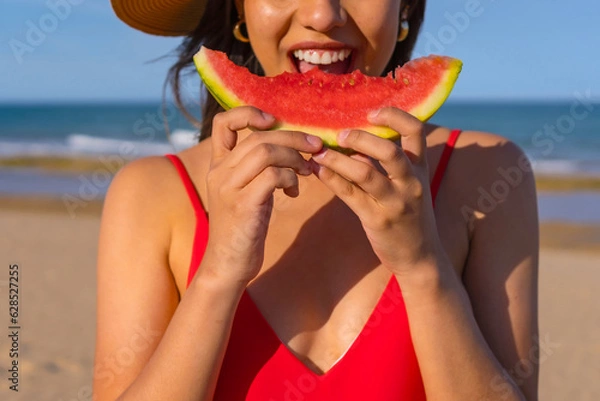 Fototapeta Portrait of a woman eating a watermelon by the beach. Cutout of mouth smiling with red bikini