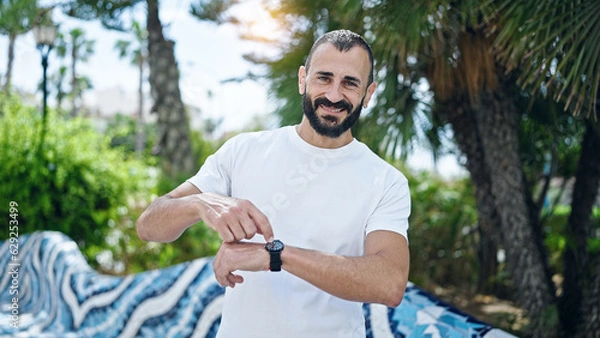 Fototapeta Young hispanic man smiling confident pointing to watch at park