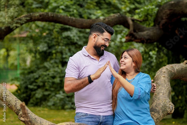 Fototapeta Young indian couple making home shape with hand at park.