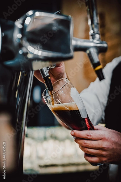 Obraz man bartender hand at beer tap pouring dark beer in glass in bar or pub