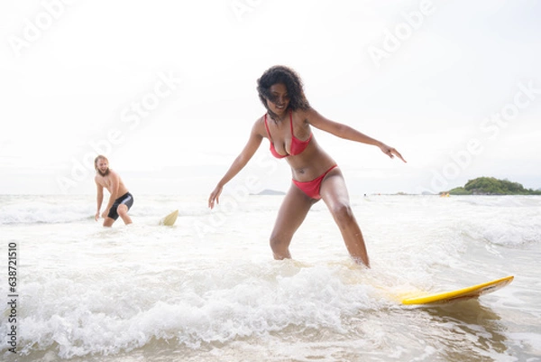 Fototapeta Couple surfing on the beach having fun and balancing on the surfboard