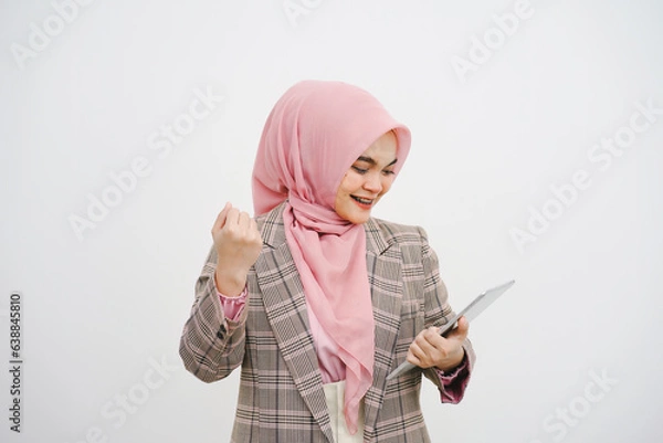 Fototapeta Portrait of a happy beautiful young muslim businesswoman pink hijab celebrating success with arms raised, fists clenched. On white background.