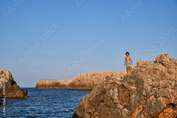 Fototapeta Boy standing on rock near blue sea