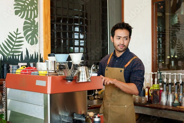 Fototapeta Portrait Nice-looking Asian man wh owns shop wearing apron, man standing making coffee according order that customer ordered standing in front coffee machine that can do all coffee menu...