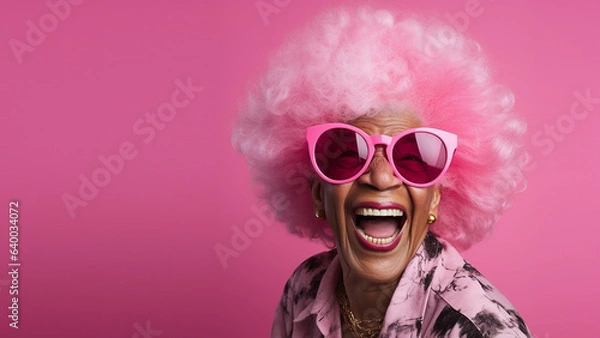 Fototapeta Happy, laughing, lovely old woman, with pink afro hair and pink sunglasses, on solid colour background, with room for text.