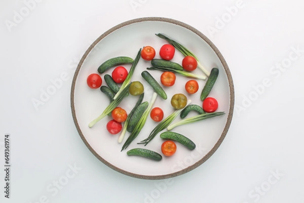 Fototapeta Tomatoes, cucumbers and green onions on a round white plate with a dark rim. Mini vegetables in a plate.