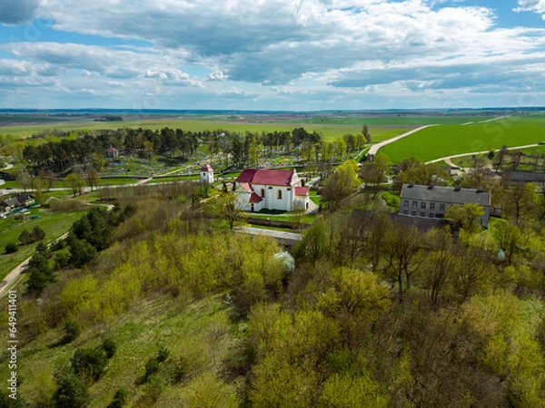 Fototapeta Aerial view over a small village near a dirt road. Large multi-colored fields planted with various agricultural crops. Wheat field from a bird's-eye view.