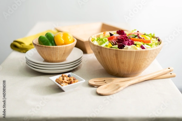 Fototapeta Healthy Vegetable Salad Featuring Bell Pepper and Lettuce in a Bamboo Bowl, Served on a Beige Fabric Tablecloth in a Bright Interior, Accompanied by a Wooden Spoon and White Dishware.