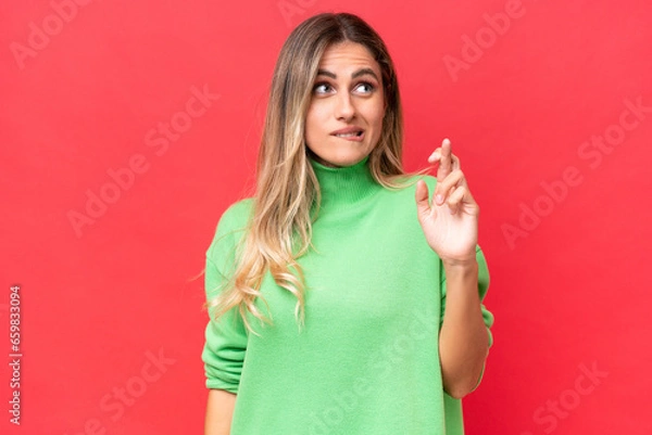 Fototapeta Young Uruguayan woman isolated on red background with fingers crossing and wishing the best