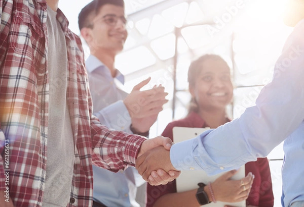 Fototapeta Young startup in casual clothes shaking hands in a modern office space by the window.