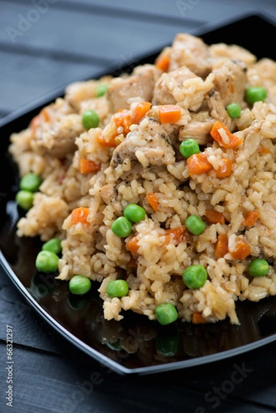 Fototapeta Pilaf with chicken, green peas and carrot in a black plate