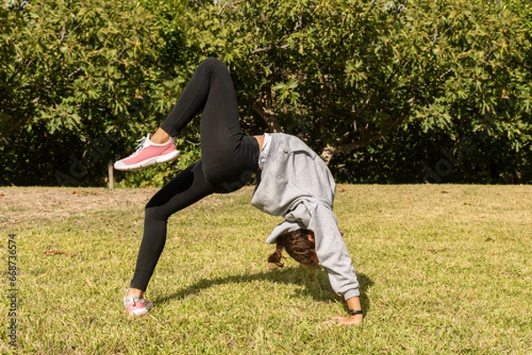 Fototapeta A girl in the park doing acrobatic exercises, playing outdoors and engaging in gymnastics activities. Healthy and sporty lifestyle