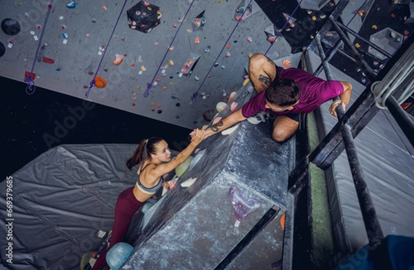 Fototapeta A strong couple of climbers climb an artificial wall with colorful grips and ropes.