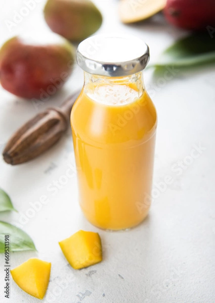 Obraz Bottle of fresh mango smoothie with pieces on light background.