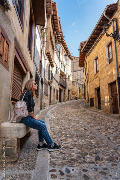 Fototapeta Tourist woman resting on a stone bench in the medieval town of Frias, Burgos, Spain.