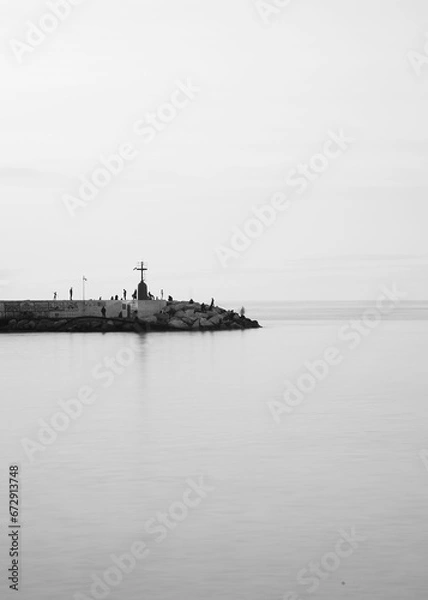 Fototapeta Tranquil body of water with people walking on a pier in the distance