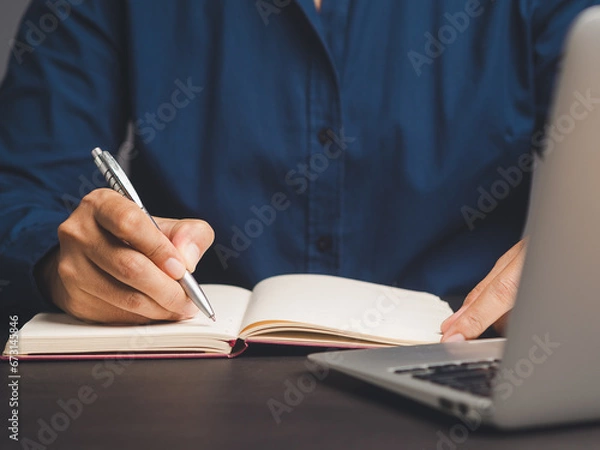 Fototapeta Businessman hand holding a pen and writing in a notebook while sitting in the office