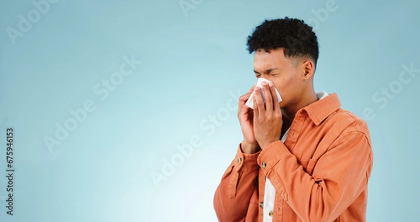 Fototapeta Man, blowing and nose for sinus in studio for healthcare mock up on blue background in Cape Town. Male model, hand and tissue for hay fever, flu or congestion for allergies with announcement in space