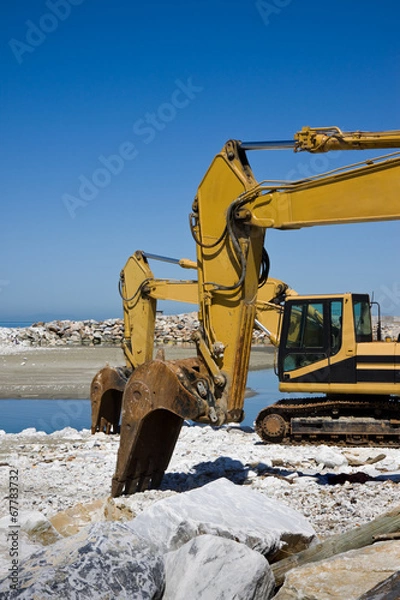 Fototapeta Yellow diggers on the seashore building a breakwater