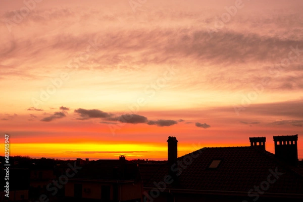 Fototapeta Roofs of houses against the backdrop of a beautiful sunset. Orange sky with beautiful cumulus clouds. Textured sky background at sunset.