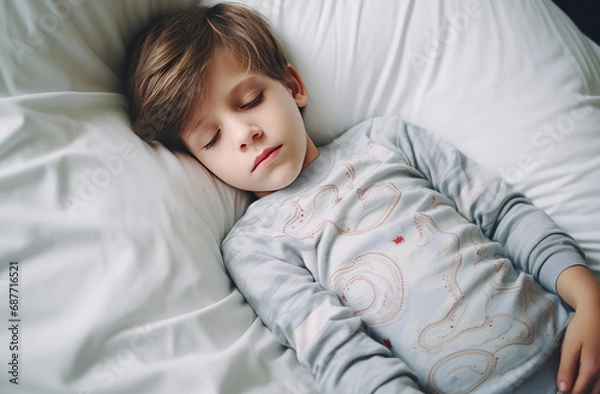 Fototapeta Sleepy pretty child boy falling asleep in his bed on clean linens, top view. Regimen for baby, lunchtime nap, children's insomnia.