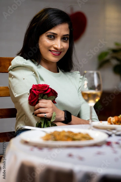 Fototapeta Vertical shot of happy girl with red roses looking at camera during candlelight dinner at restaurant - concept of valentines day, anniversary and dating