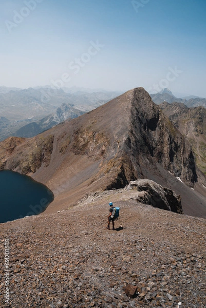 Fototapeta Vertical shot of a mountaineer descending towards the Ibón and Pico de Tebarray in the Pyrenees of Huesca during summer