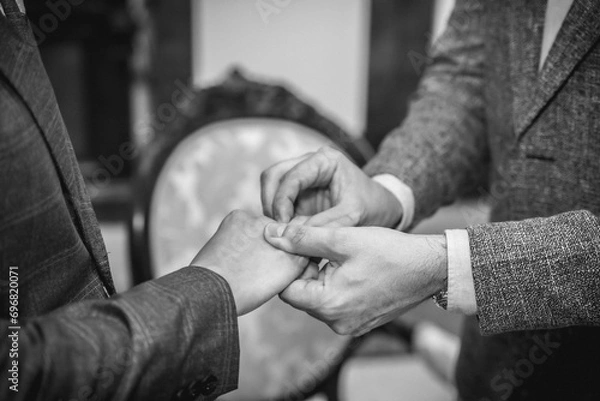 Fototapeta Gay wedding groom placing ring on husband at ceremony, gay marriage, lgtb concept, black and white photo