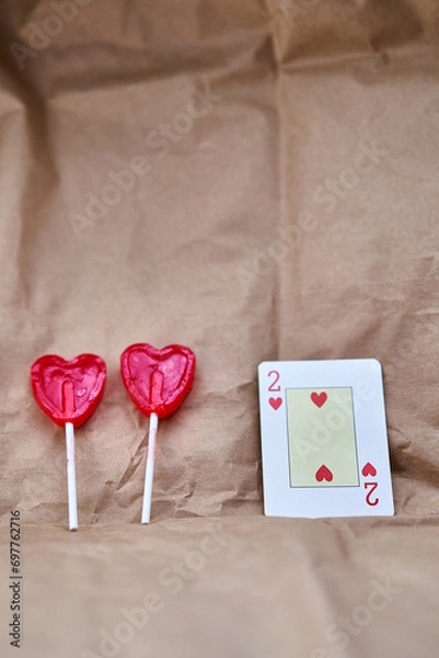 Fototapeta Two red heart-shaped lollipops and a two hearts card on a cardboard background.