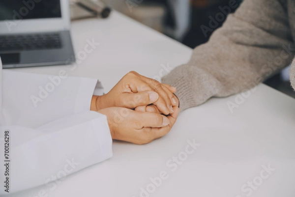 Fototapeta Doctor and patient sitting near each other at the table in clinic office. The focus is on female physician's hands reassuring woman, only hands, close up. Medicine concept