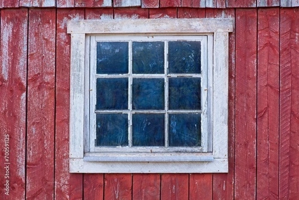 Fototapeta Closeup of a white framed window on a red painted old wooden building.